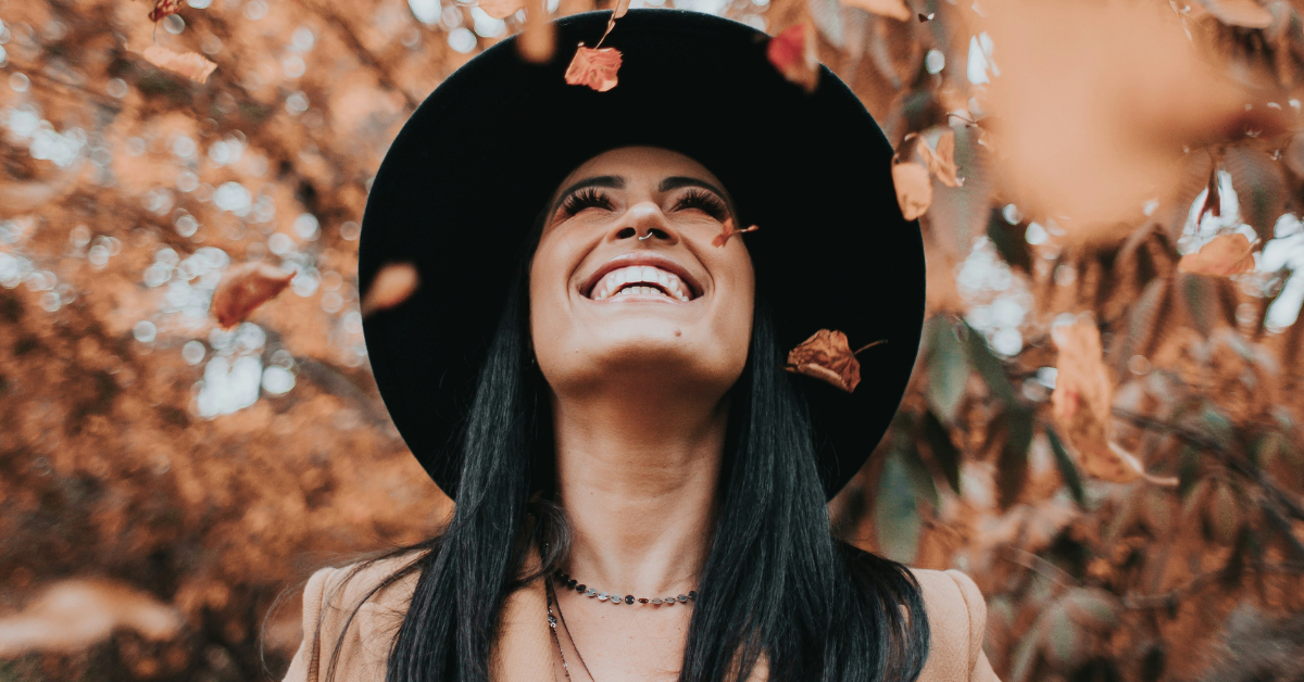 Woman throwing leaves wearing a fall transition outfit