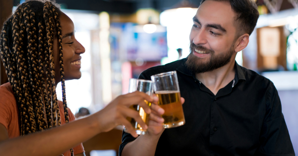 Young interracial couple meeting in a bar clinking beers off a dating app