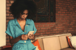 Beautiful Black woman looking sadly at cellphone and experiencing dating app burnout